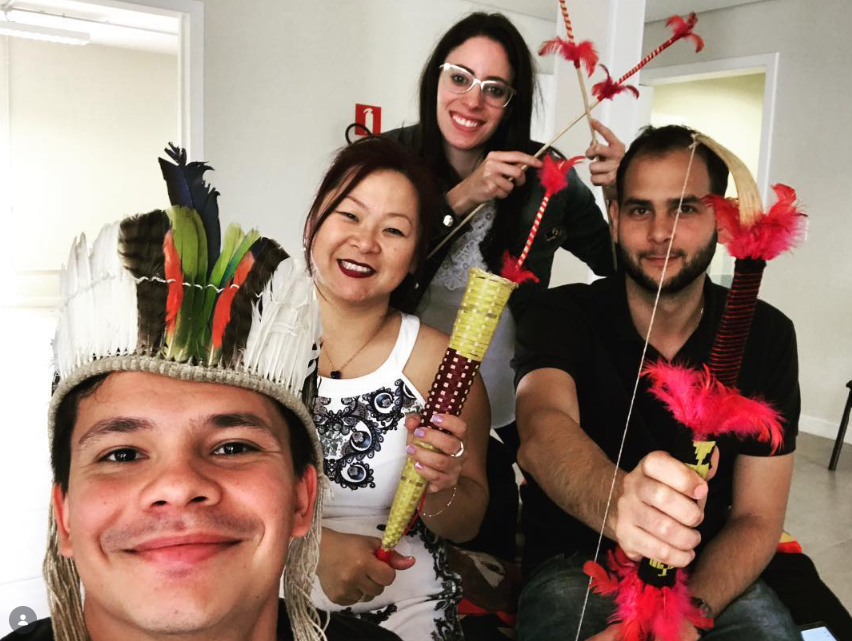 Marcos e equipe com cocar e arco-e-flecha indígenas, em visita a aldeia