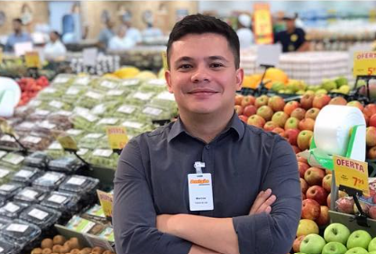 Marcos de crachá, de braços cruzados, na seção de hortifrúti do supermercado