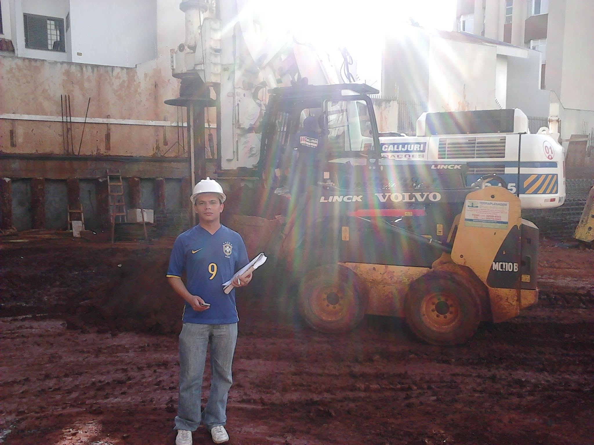 Marcos de capacete em canteiro de obra, ao lado de perfuratriz de estacas